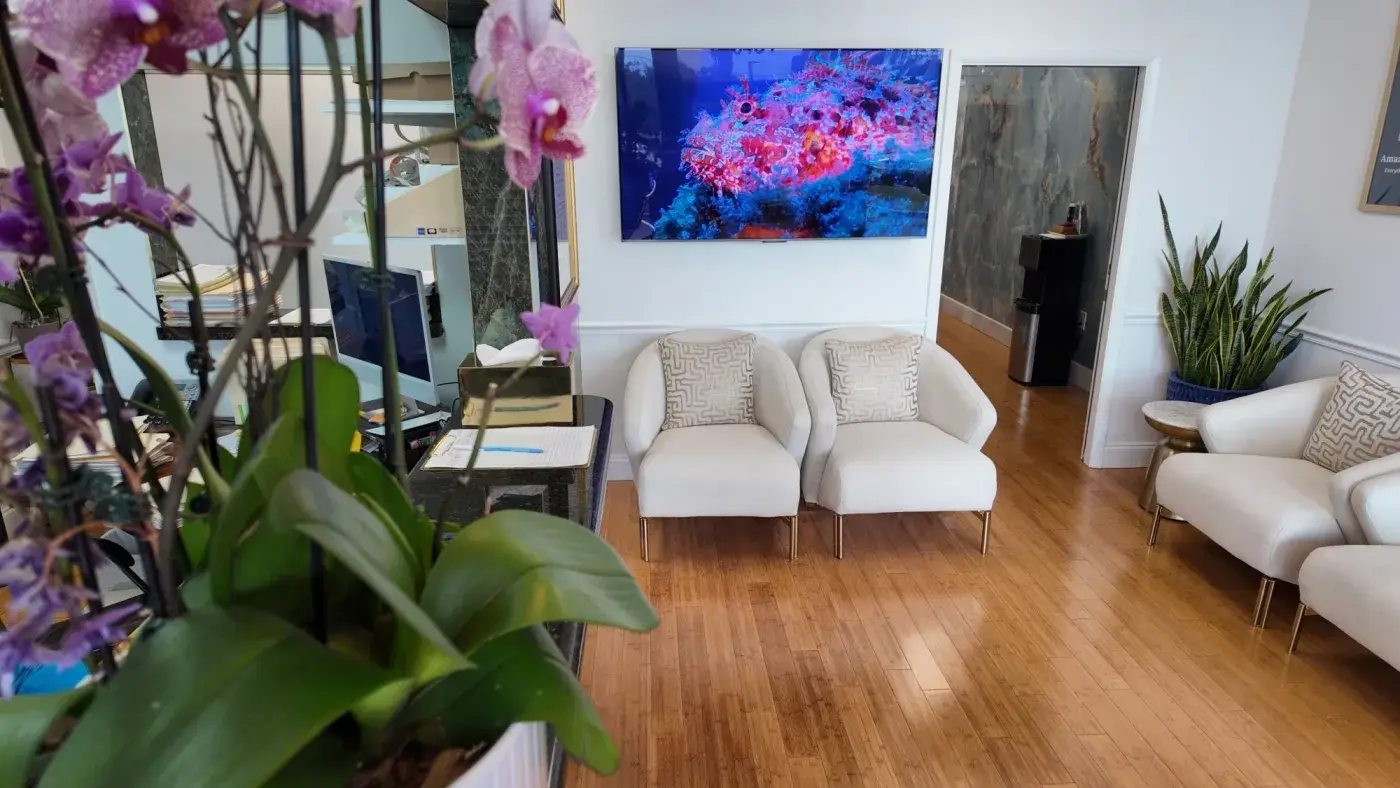 The waiting room at Luxury Chiropractic, with upholstered chairs, orchids at the front desk and a reef film on the wall screen.