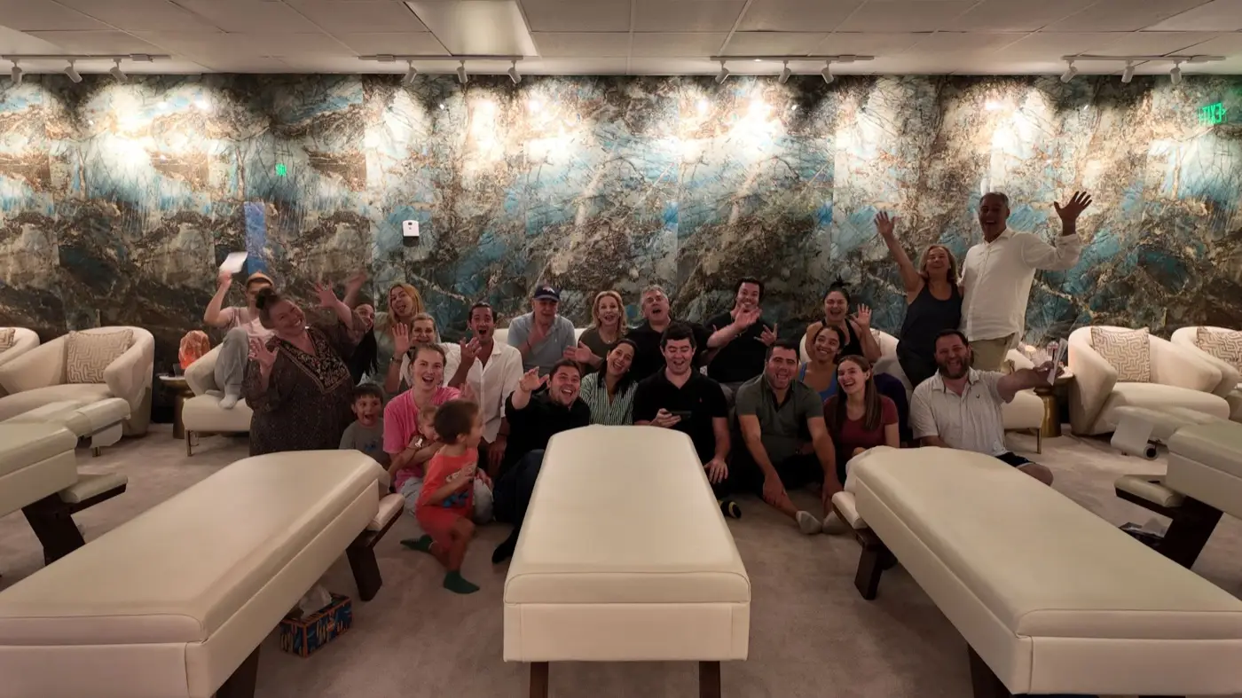 Podcast Patients and families gathered between the treatment tables in the clinic, in front of a lit blue and gold marble wall.